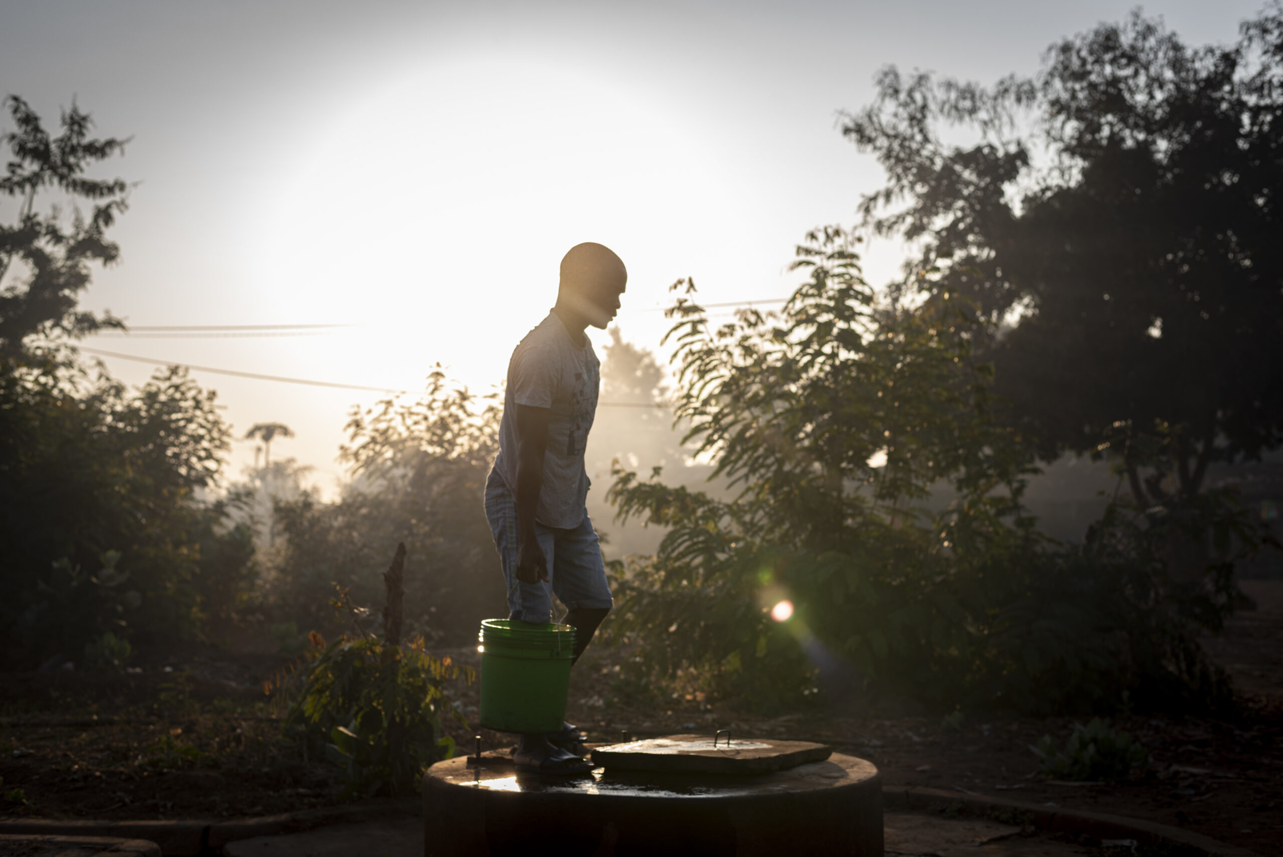 Credit: WaterAid/ Etinosa Yvonne. A young man carries a bucket of water he fetched from a well. The water is used at the health centre in Napacala